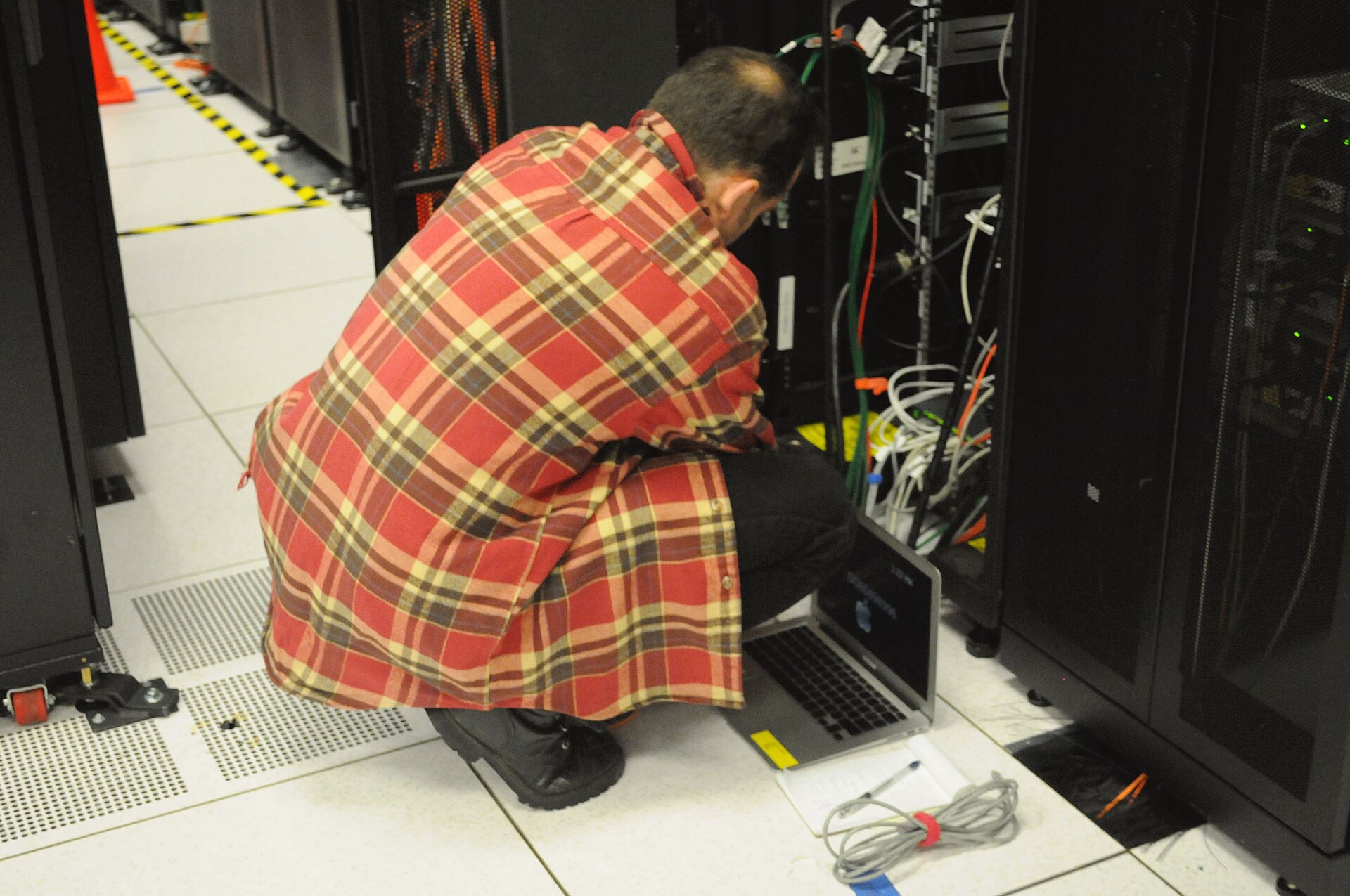 Le compute finit toujours quelque part: dans des racks, des câbles et des gens qui doivent intervenir. Technicien devant des racks serveur au NERSC
